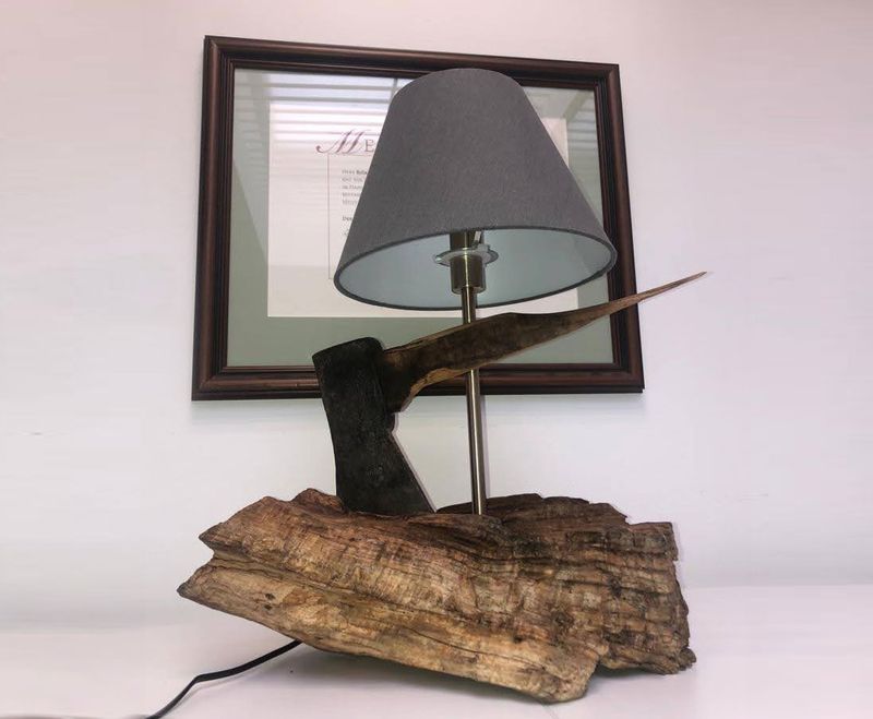 Eine einzigartige Lampe mit einem Holzsockel und einem Axtkopf, der von einem grauen Stoffschirm gekrönt wird